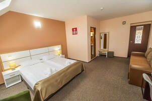 Habitación de hotel con cama, mesitas de noche, una silla, un sofá y una puerta con panel decorativo.