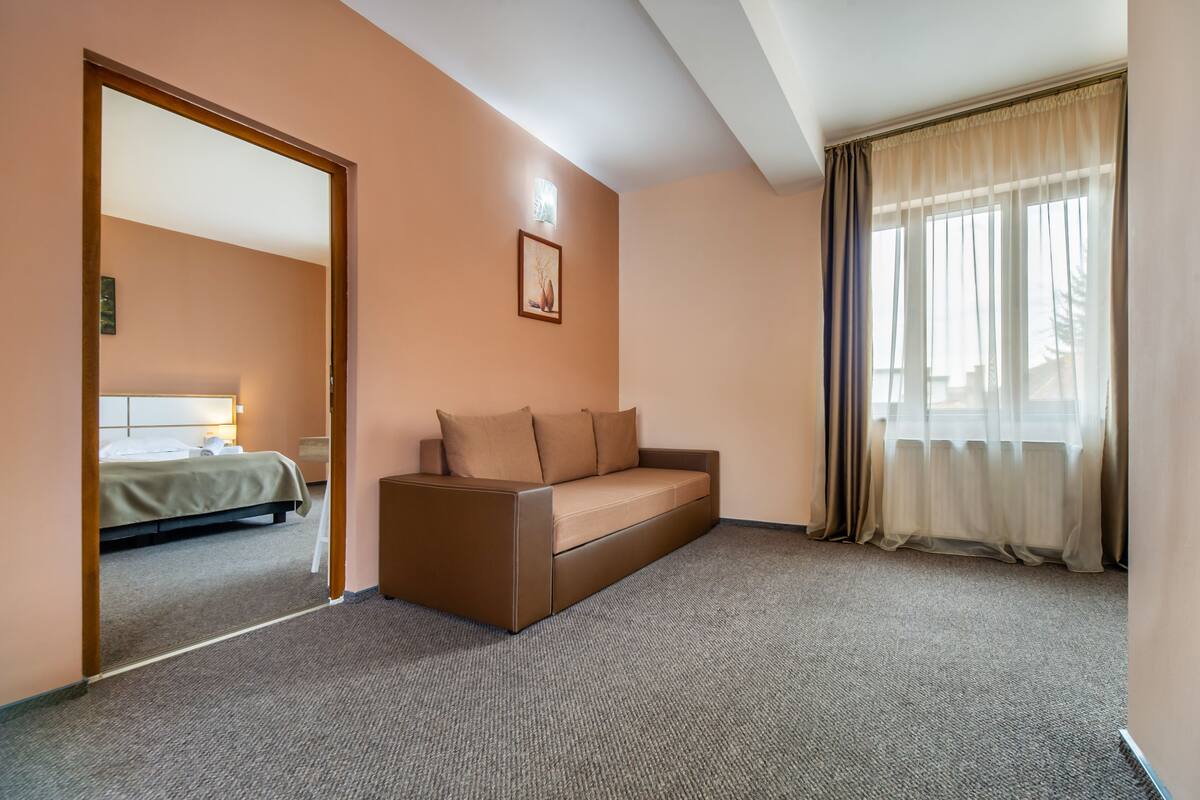 A hotel room with a bed, a sofa, a picture on the wall, and a window with curtains.