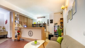 A reception area with a counter, a sofa, and a table with a vase. - Long Street Hotel (Brasov)