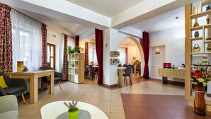 A spacious living area with a dining table, chairs, and a sofa. There are bookshelves and a small kitchen area in the background. - Long Street Hotel (Brasov)