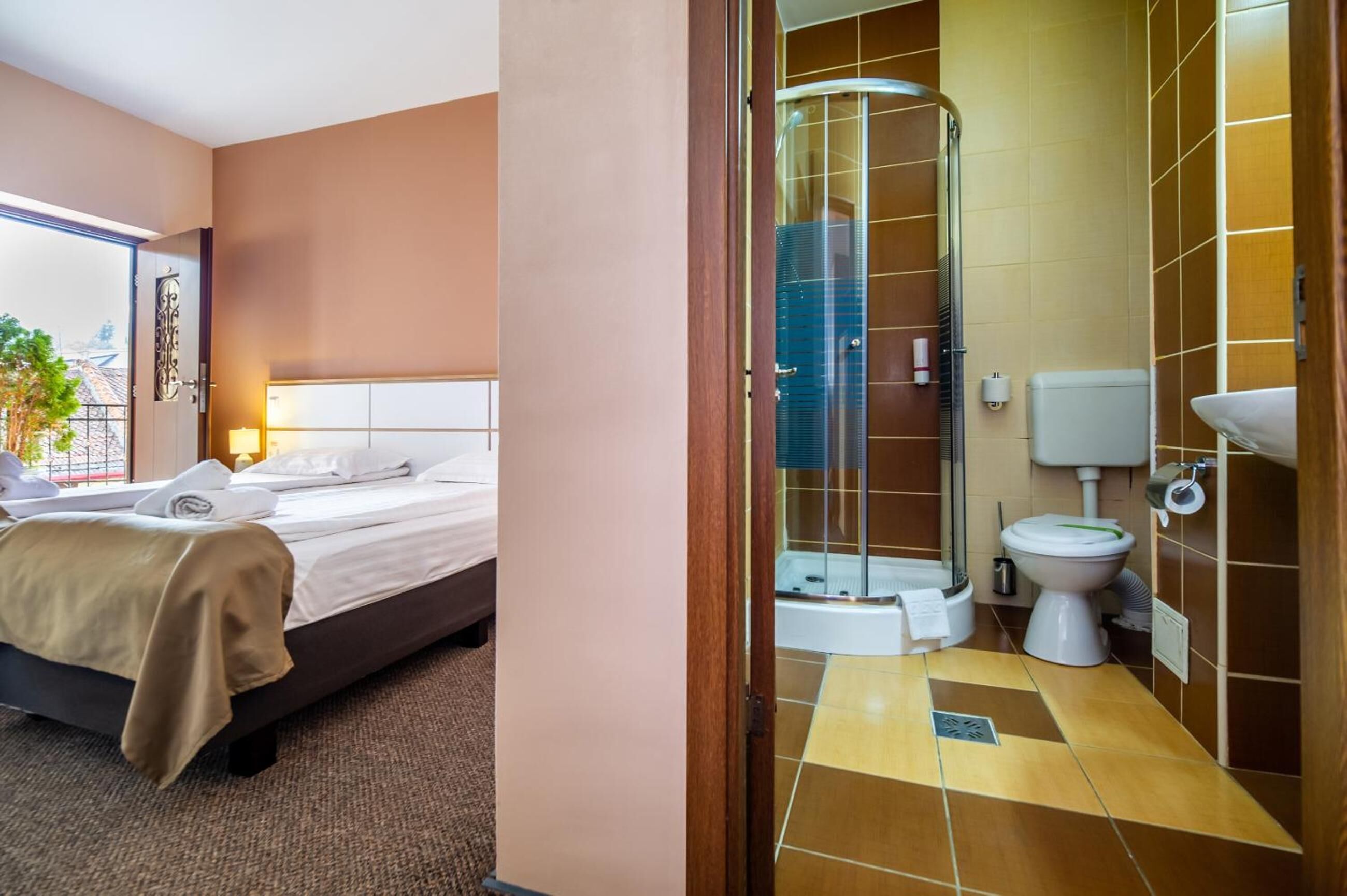 A hotel room with a bed, a bathroom with a shower, and a toilet.