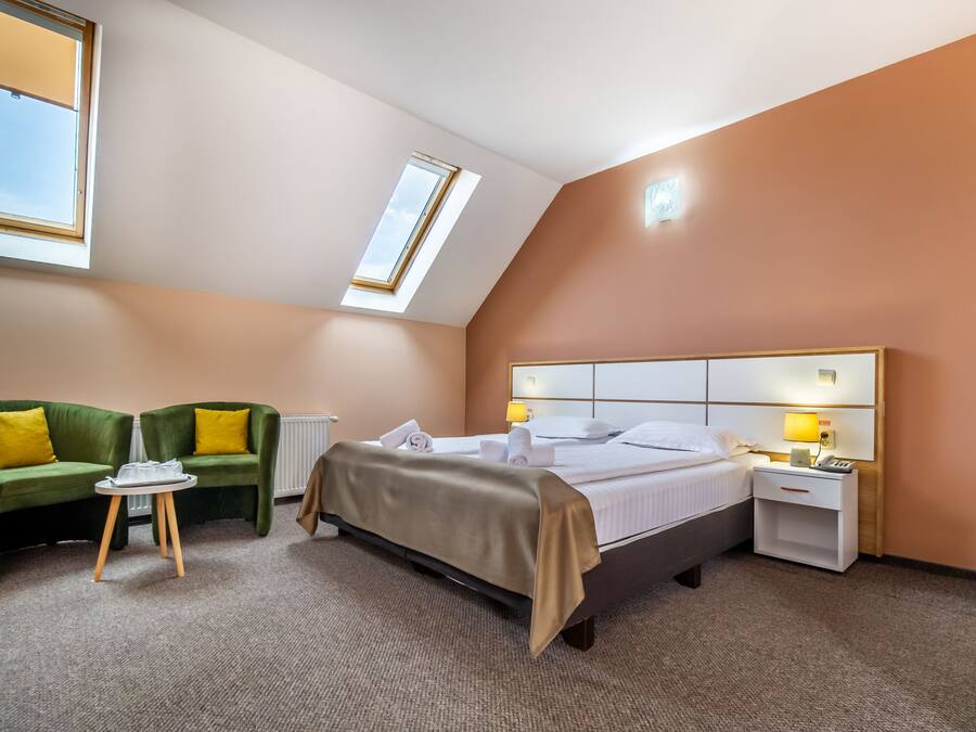 A hotel room with a bed, a green sofa, a small table, a nightstand, and a skylight.
