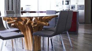 A dining area with a unique wooden table centerpiece, modern chairs, and a kitchen in the background. - Pebbles Boutique Aparthotel (Sliema)