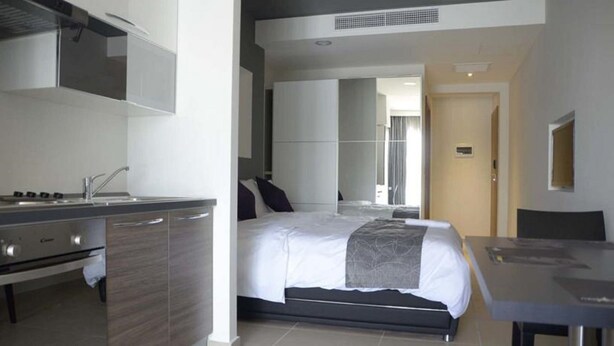 A modern hotel room with a kitchenette, a large bed, a separate dining area, and a bathroom visible through an open door. - Pebbles Boutique Aparthotel (Sliema)