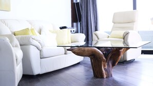 A modern living room with a white sofa, a glass coffee table with a wooden base, and a white armchair. - Pebbles Boutique Aparthotel (Sliema)