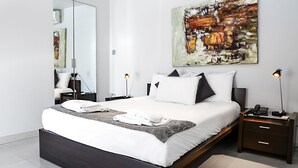 A modern bedroom with a large bed, bedside tables, a mirror, and abstract art on the wall. - Pebbles Boutique Aparthotel (Sliema)