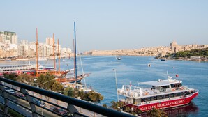 A harbor with boats, including a red and white ship named "Captain Morgan Cruises," and a cityscape with buildings in the background. - Pebbles Boutique Aparthotel (Sliema)