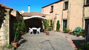 A courtyard with stone flooring, a covered seating area with two white chairs, and potted plants. - Sa Dom'e Forru (Collinas)