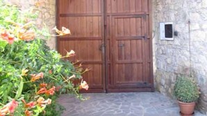 A stone wall entrance with a wooden double door, a potted plant, and a small light fixture. - Sa Dom'e Forru (Collinas)