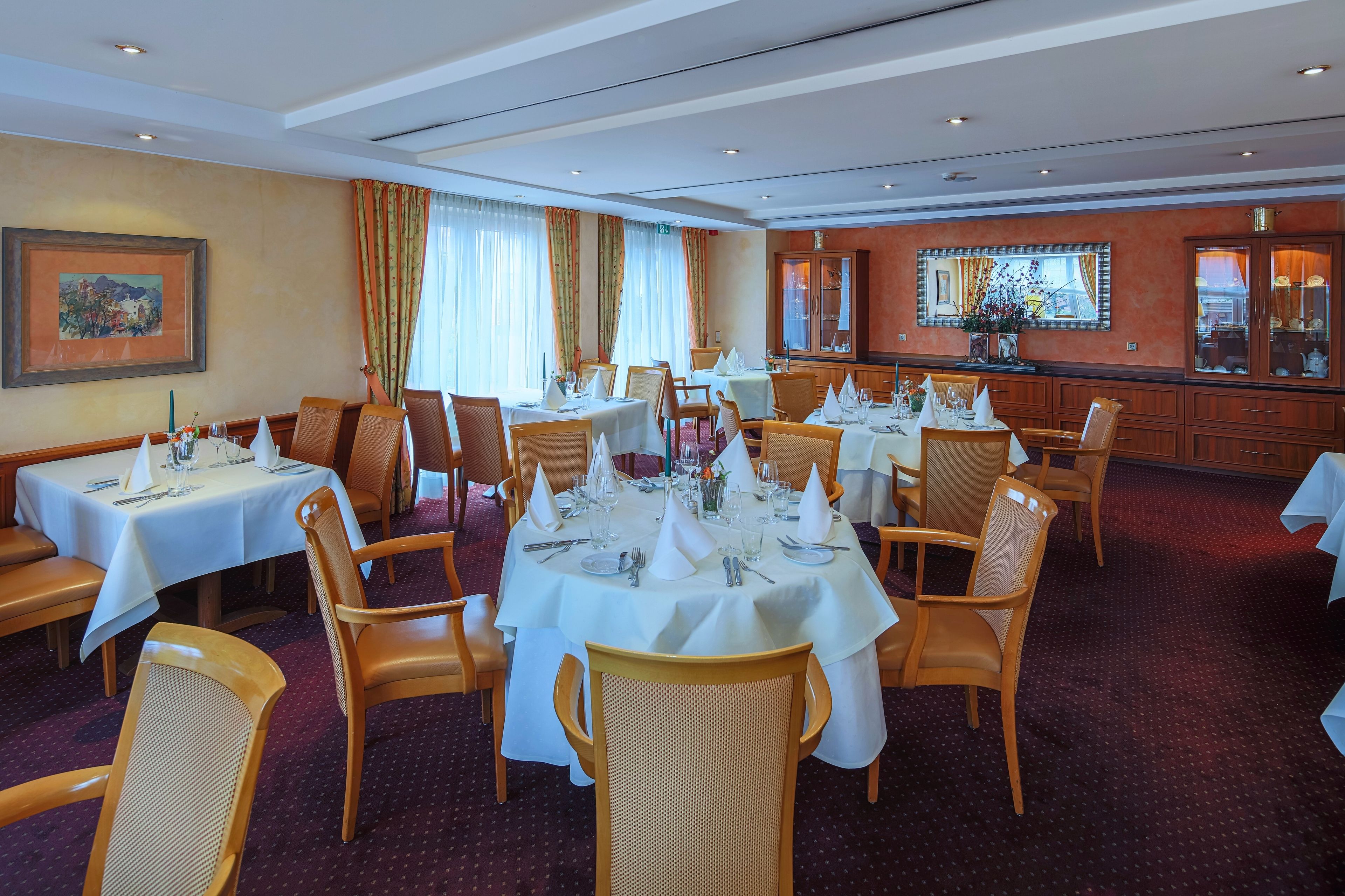 A dining area with multiple tables set for guests, featuring white tablecloths and neatly arranged cutlery.
