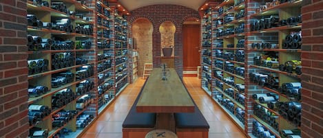 A wine cellar with shelves stocked with bottles, a central table, and a brick wall.