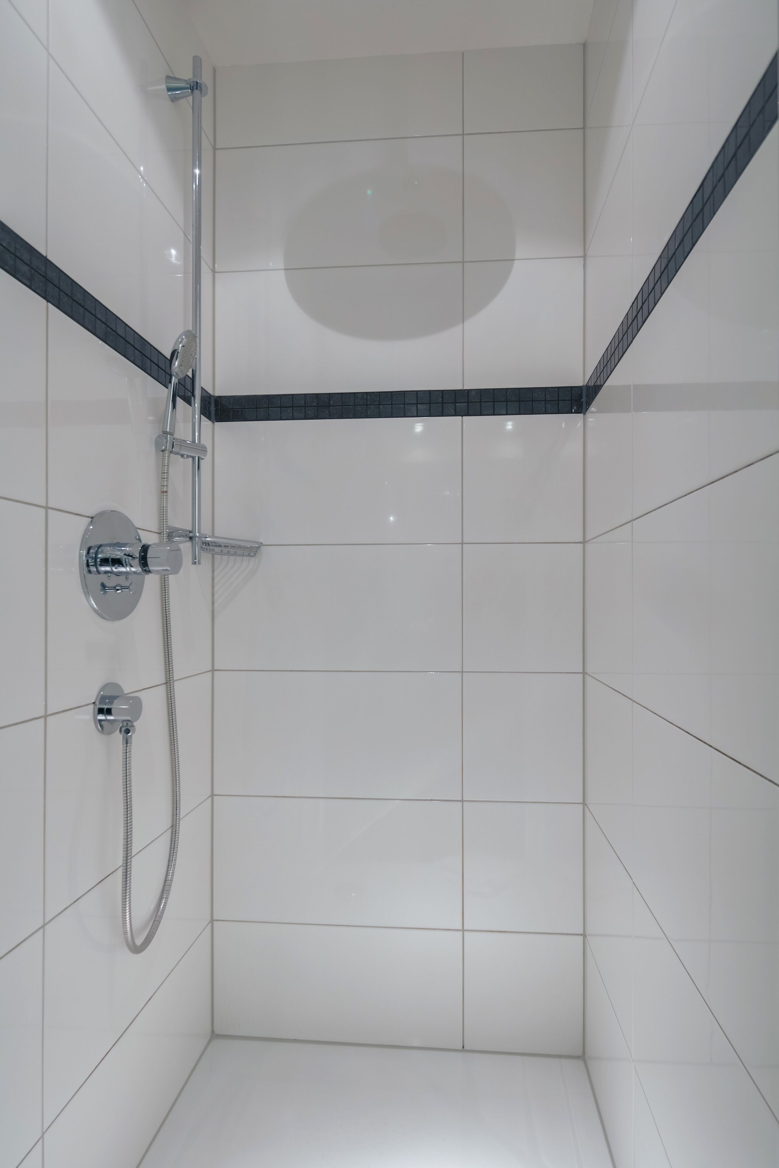 A small, tiled shower room with a handheld showerhead and a wall-mounted faucet.