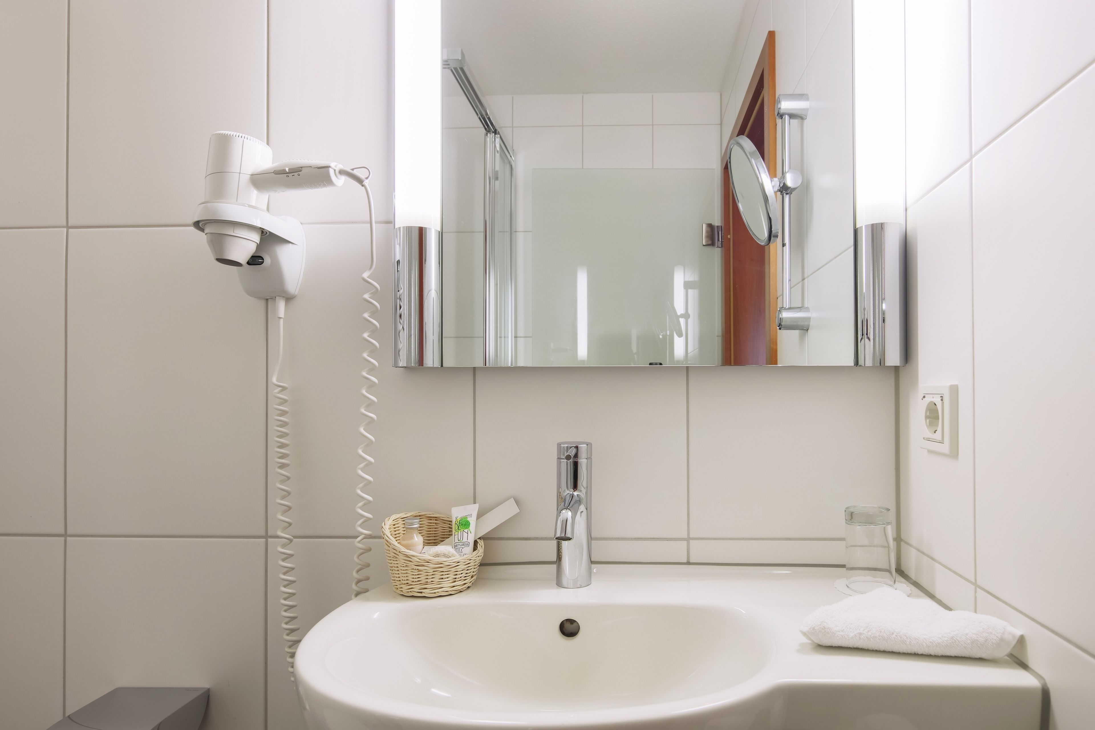 A bathroom with a white sink, a mirror, a hairdryer, and a towel.