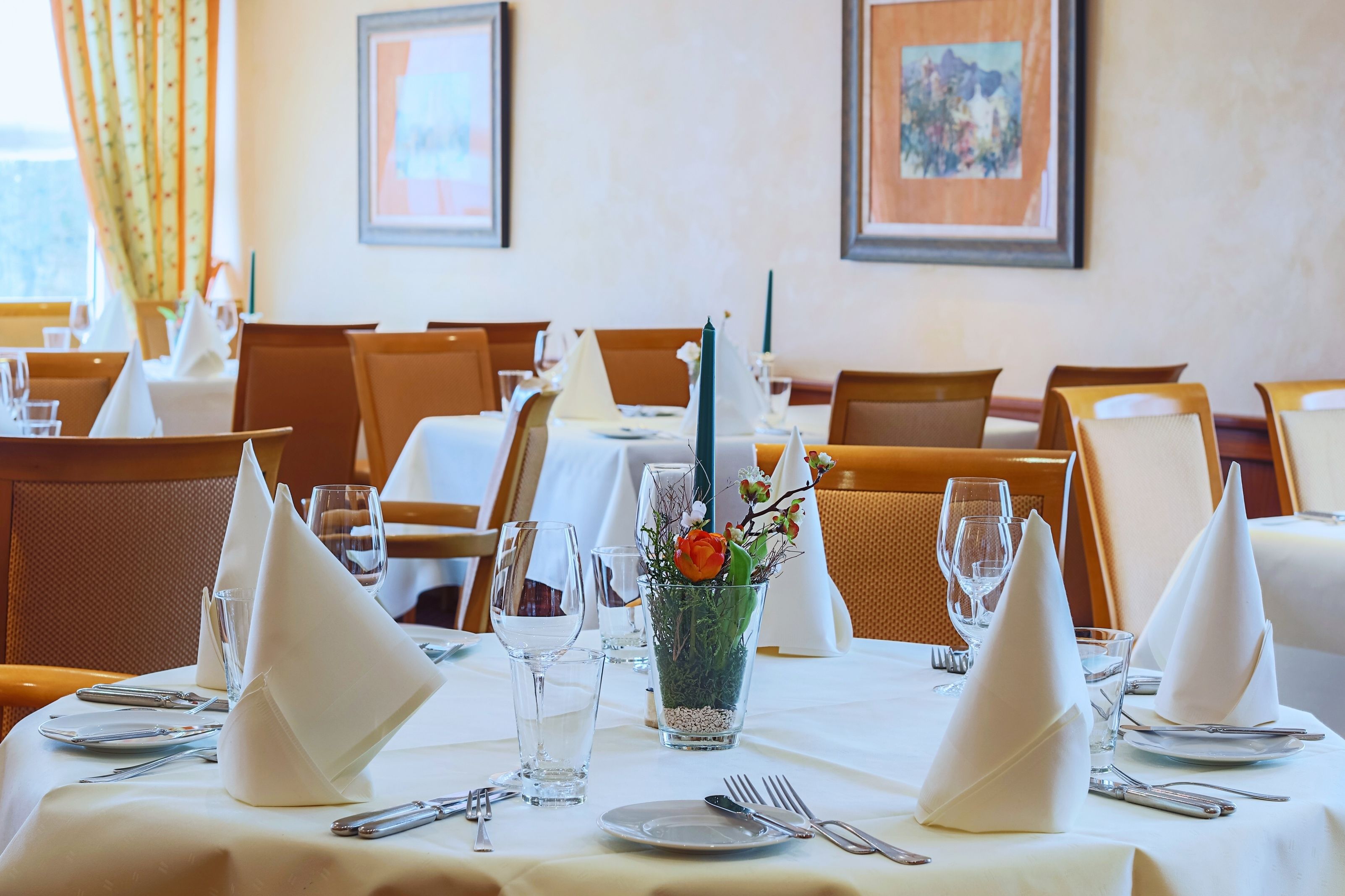 A dining table set with white napkins, silverware, and a glass vase with flowers.