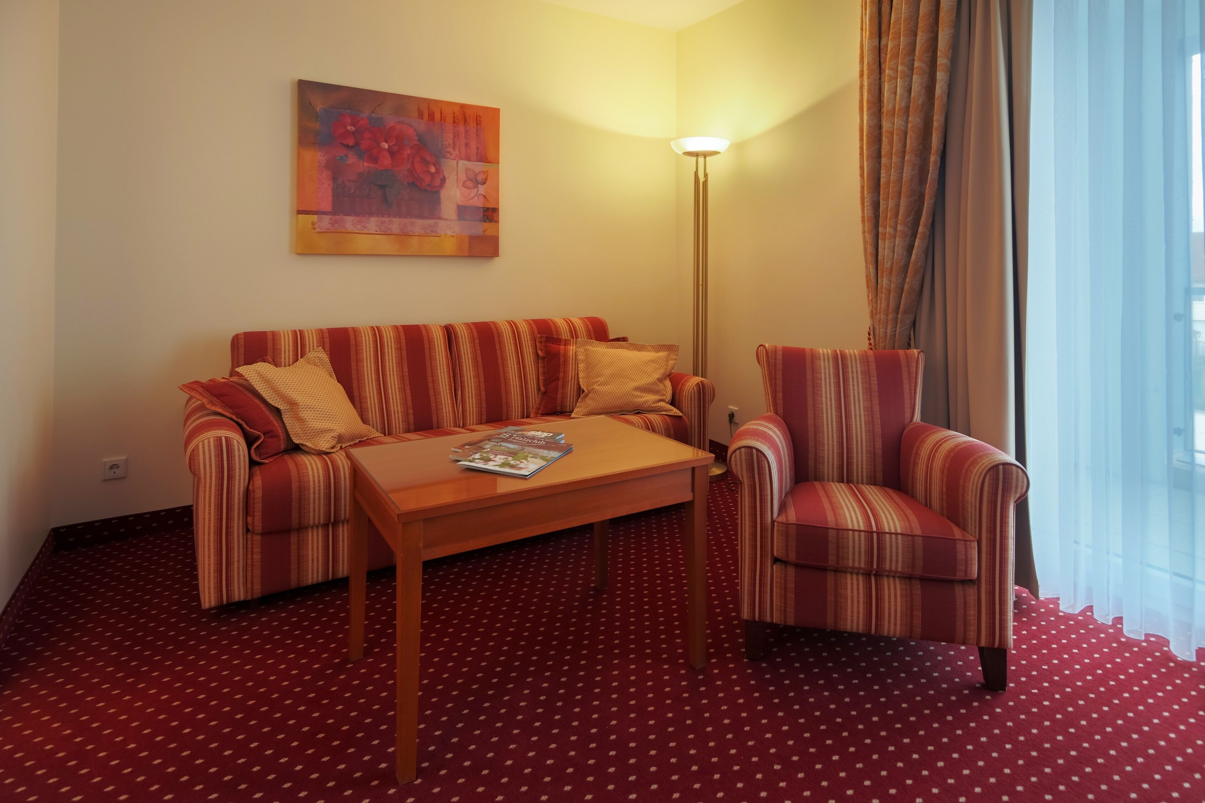 A hotel room with a striped sofa, a striped armchair, a wooden coffee table, and a floor with a red pattern.