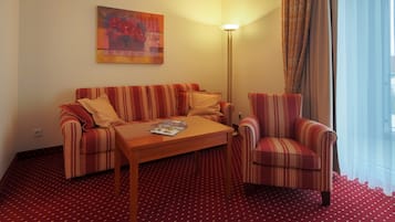 A hotel room with a striped sofa, a striped armchair, a wooden coffee table, and a floor with a red pattern.