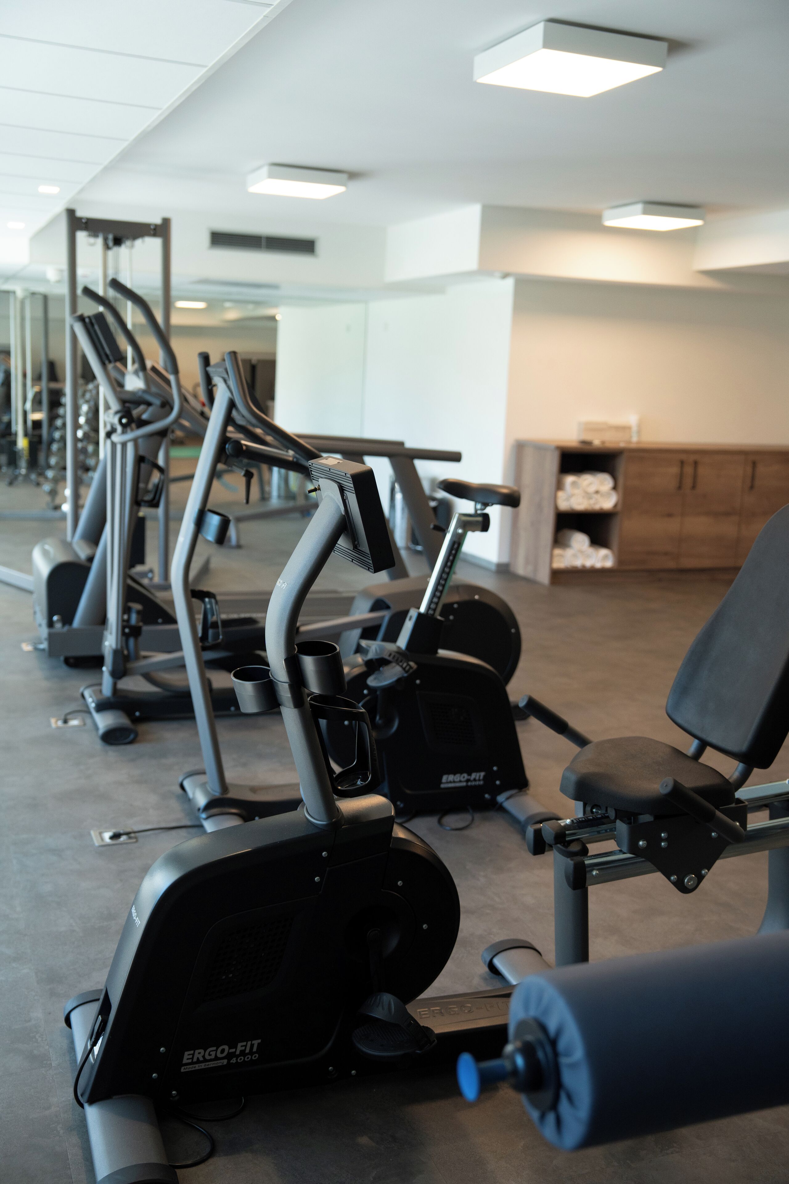 A gym with various exercise machines, including treadmills and elliptical trainers, arranged in rows.