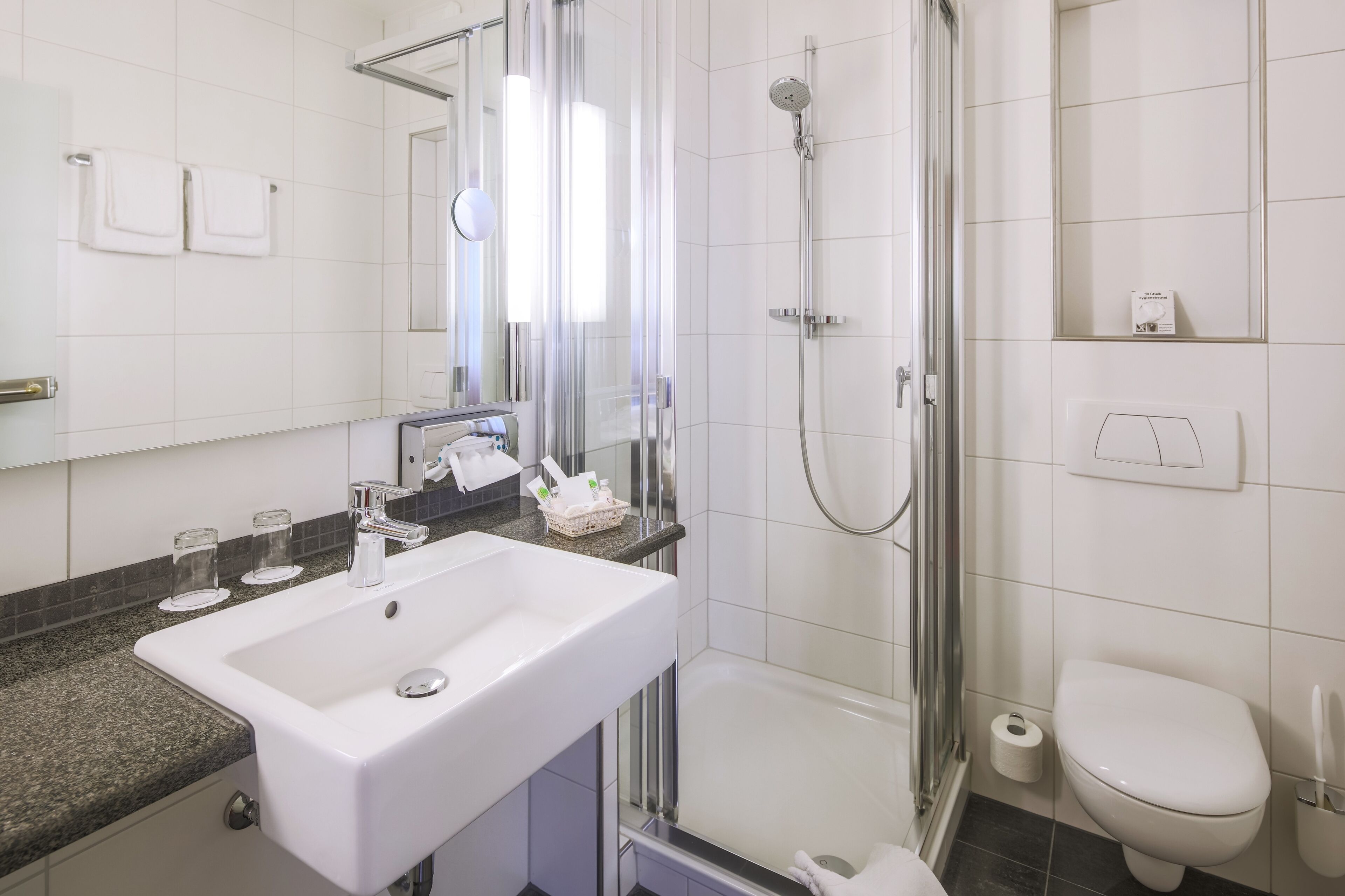 A modern bathroom with a white sink, glass shower enclosure, and a toilet.