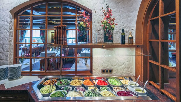 Een buffet met diverse gerechten, een raam met gordijnen en een houten plank met flessen.