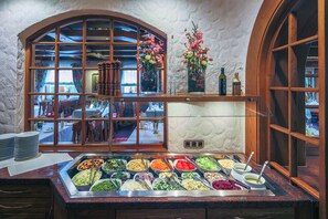 Un bufé con diversas opciones de comida, una ventana con cortinas y una estantería de madera con botellas.