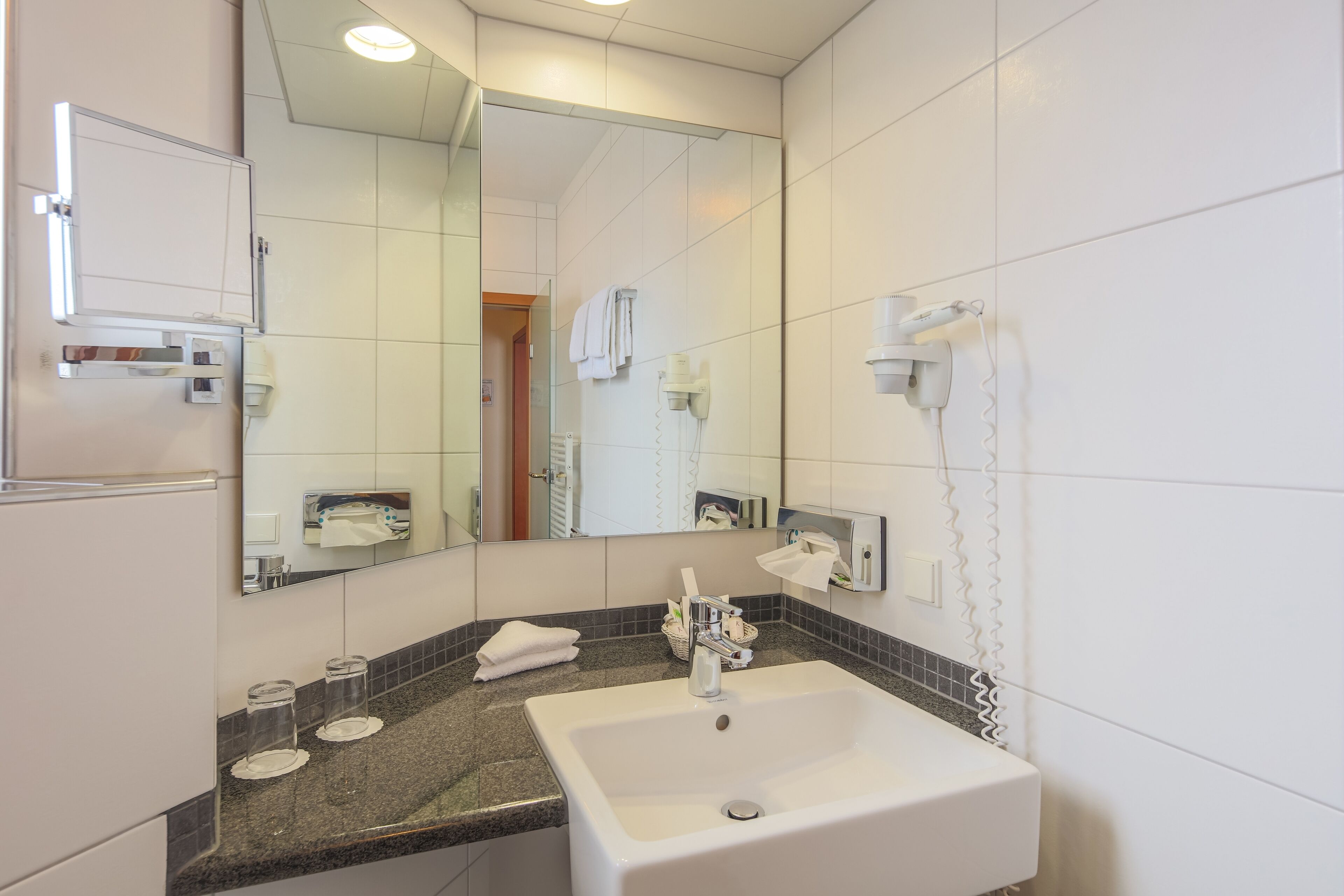 Un baño moderno con un espejo grande, un lavamanos y un secador de pelo montado en la pared.