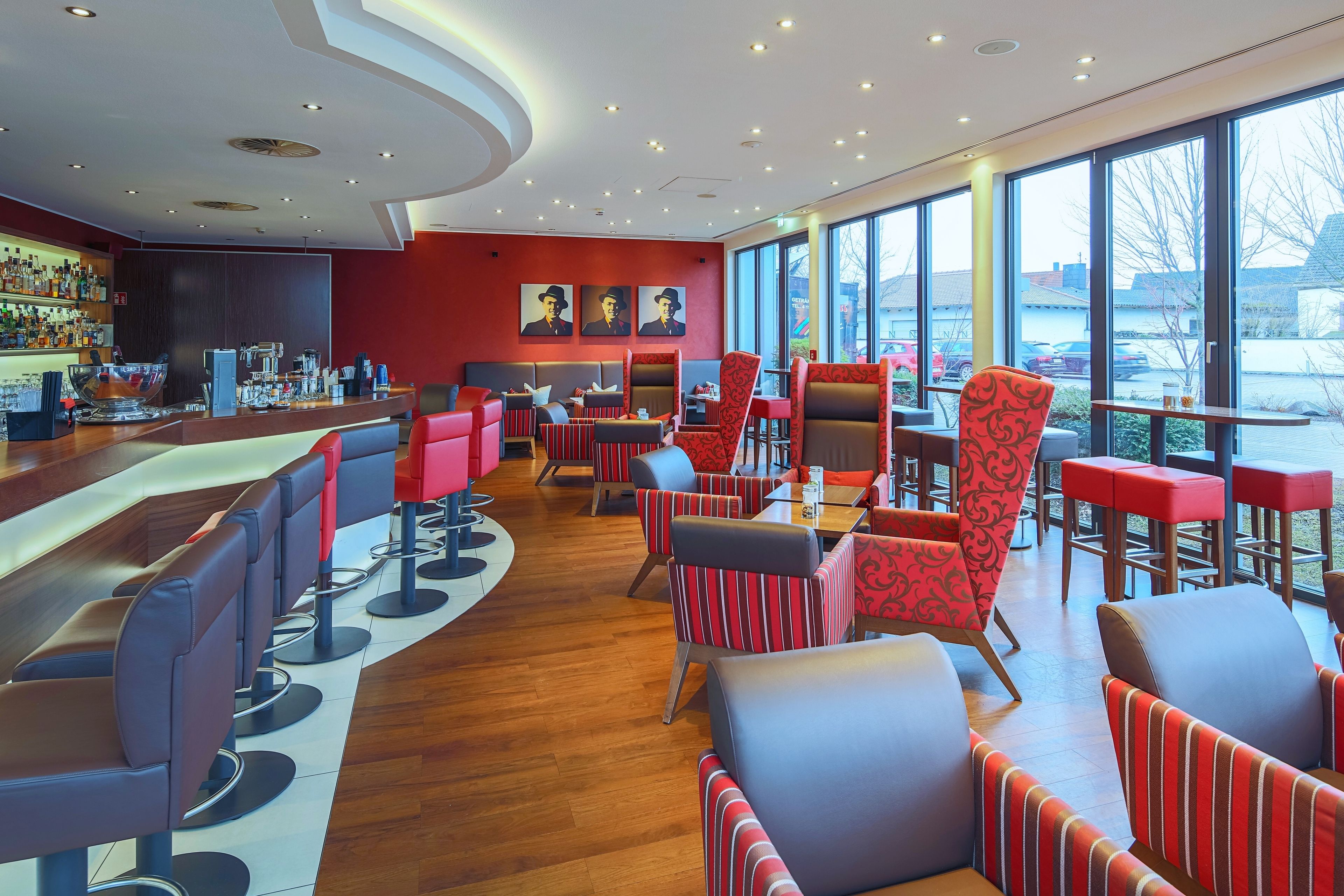 Un espace bar moderne doté d’un long comptoir, de tabourets et d’une grande fenêtre donnant sur l’extérieur.
