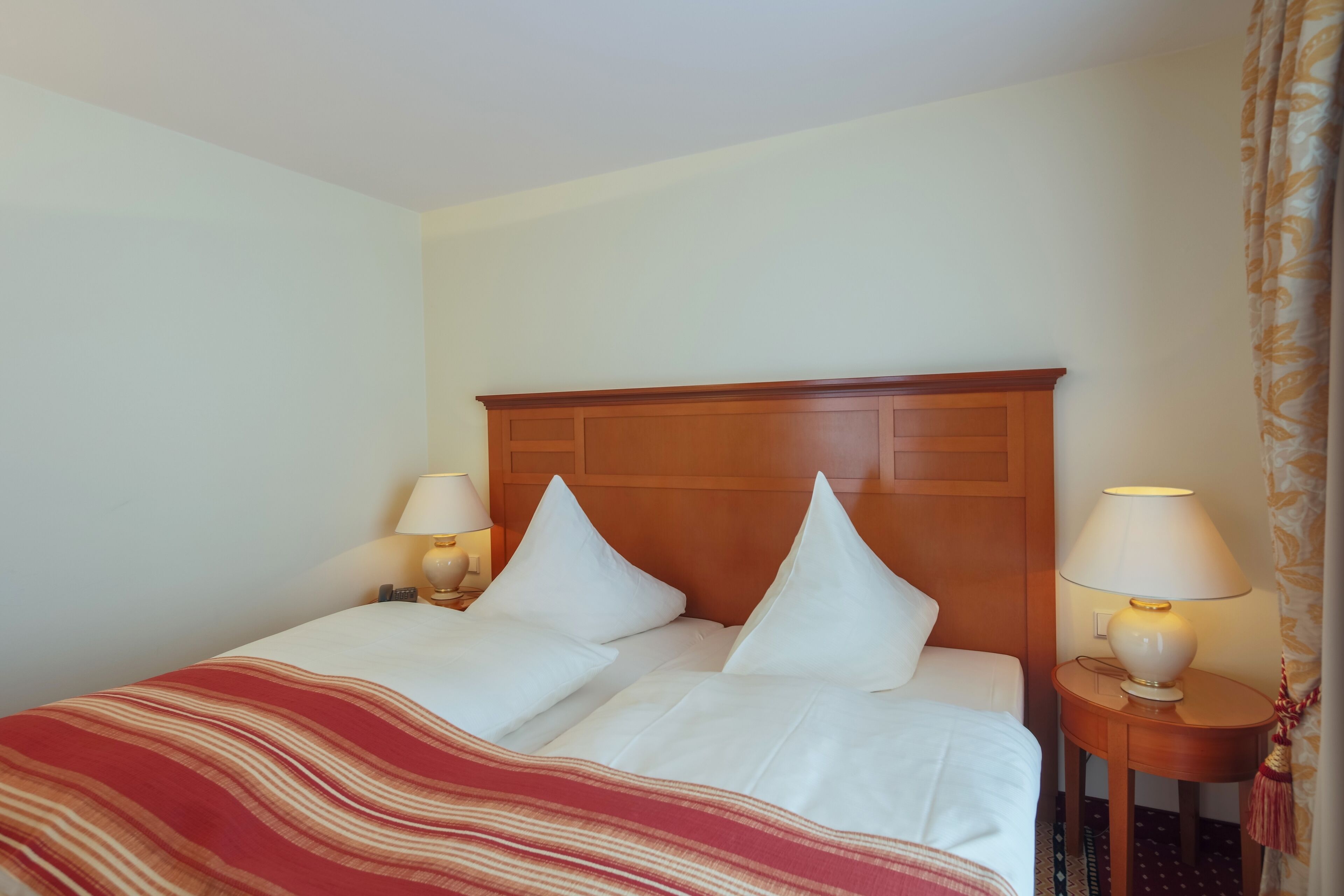 A hotel room with a large bed, two bedside lamps, and a wooden headboard.