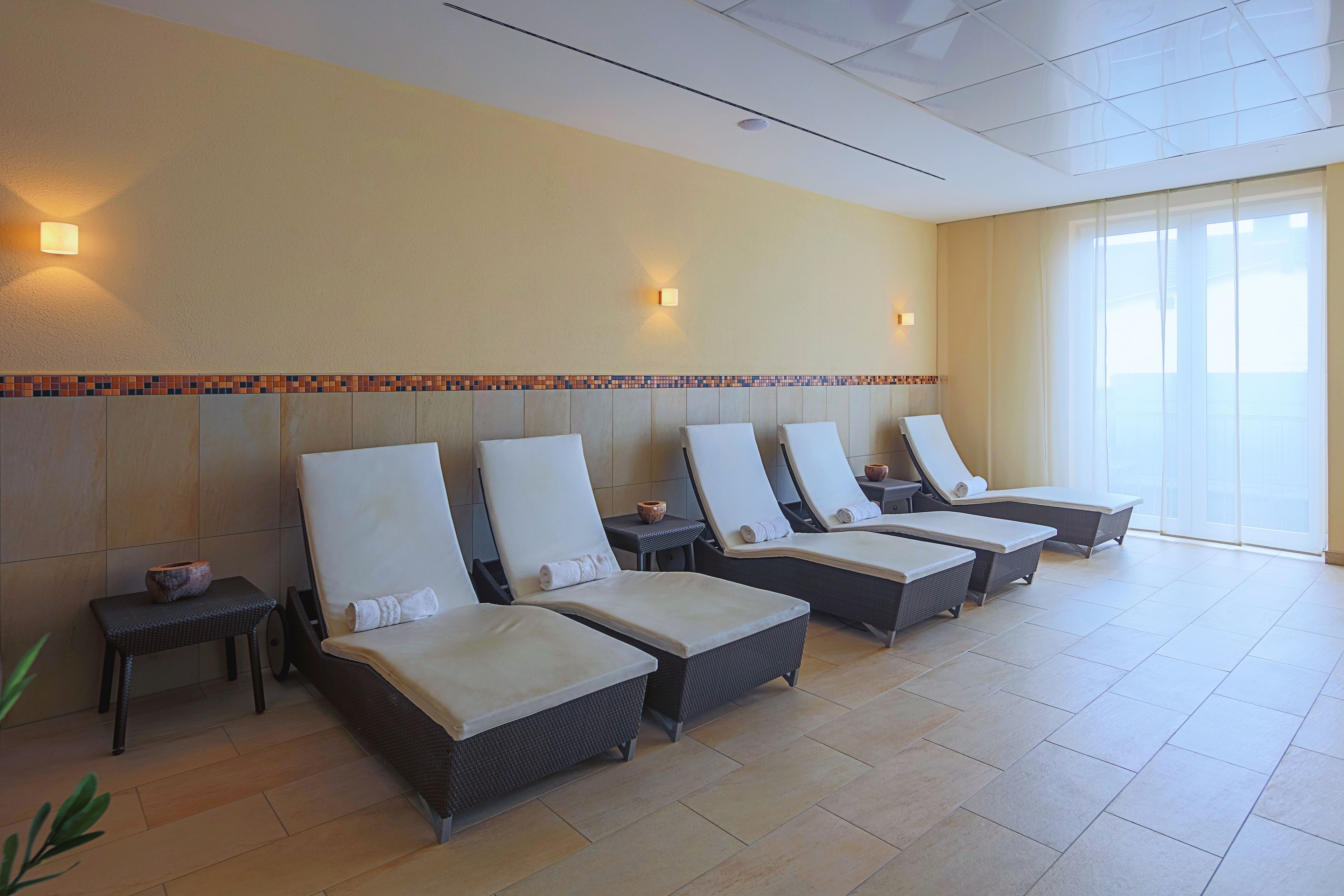 Un cuarto de spa con seis sillas reclinables dispuestas contra una pared, cada una con una mesita y un cuenco decorativo.