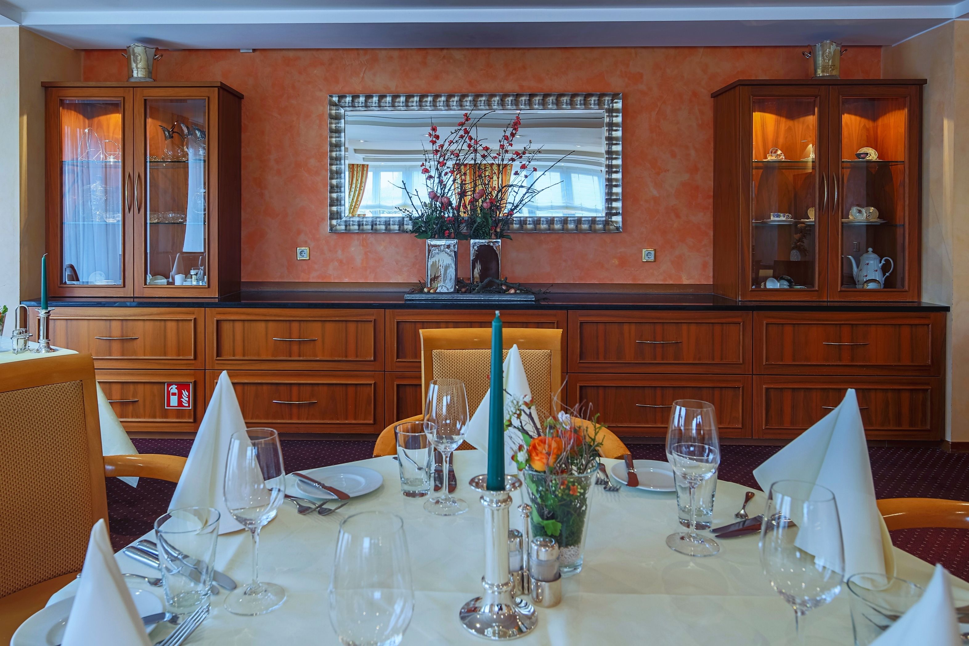 A dining area with a table set for two, featuring a vase with flowers, a candle, and a mirror above the table.