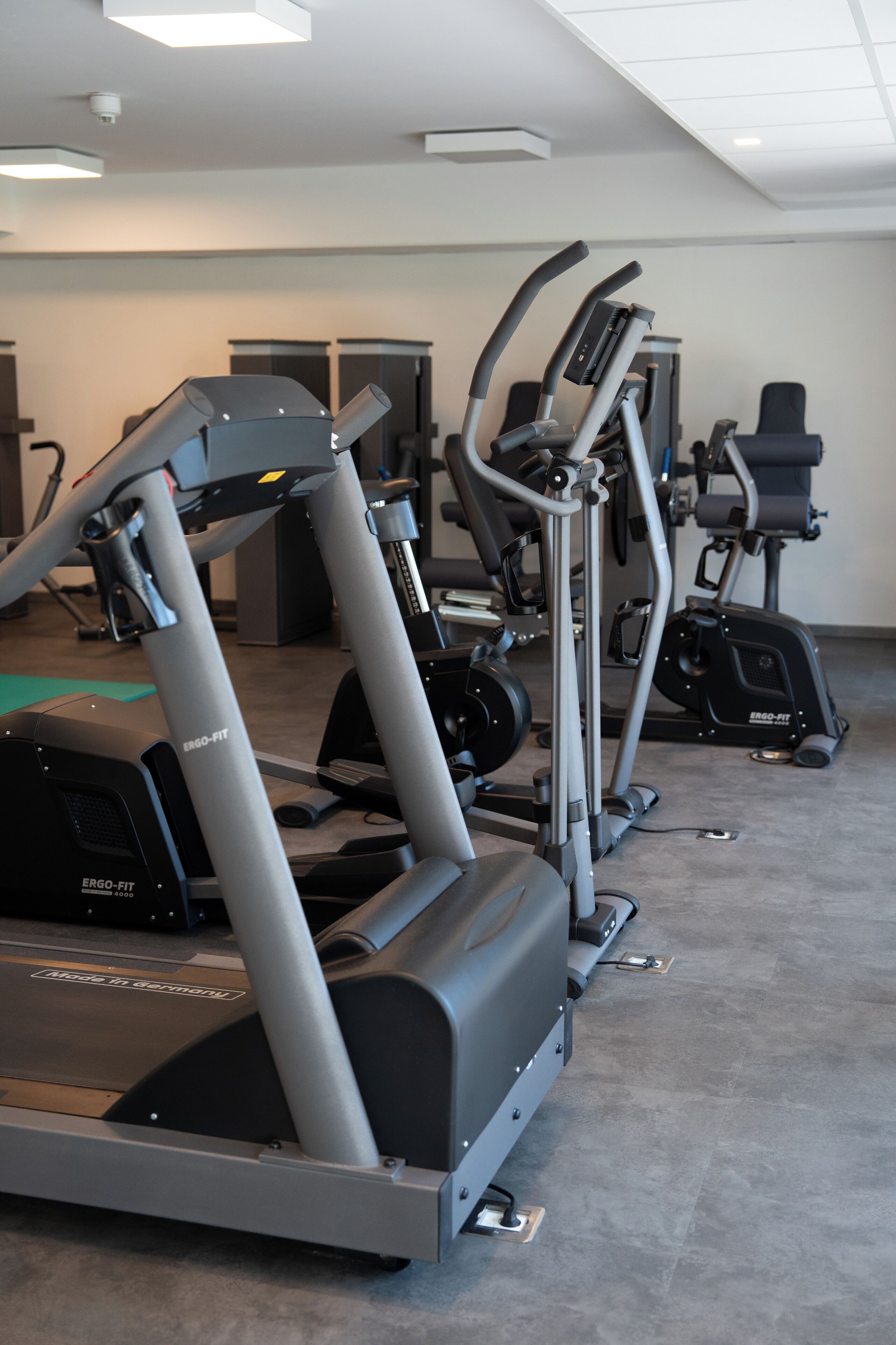 Un gimnasio con diversas máquinas de ejercicio, incluyendo cintas de correr y elípticas, dispuestas en fila.
