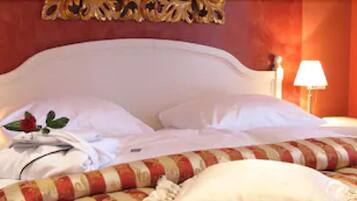 Una cama bien hecha con sábanas blancas y una manta a rayas, dos lámparas de noche y un objeto decorativo en la mesita.