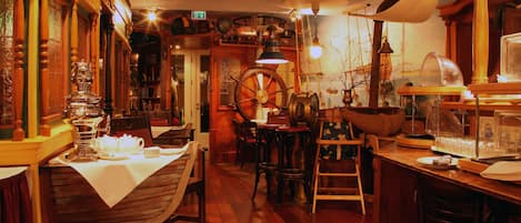 A cozy restaurant interior with wooden furniture, a large wooden wheel, and vintage decor.