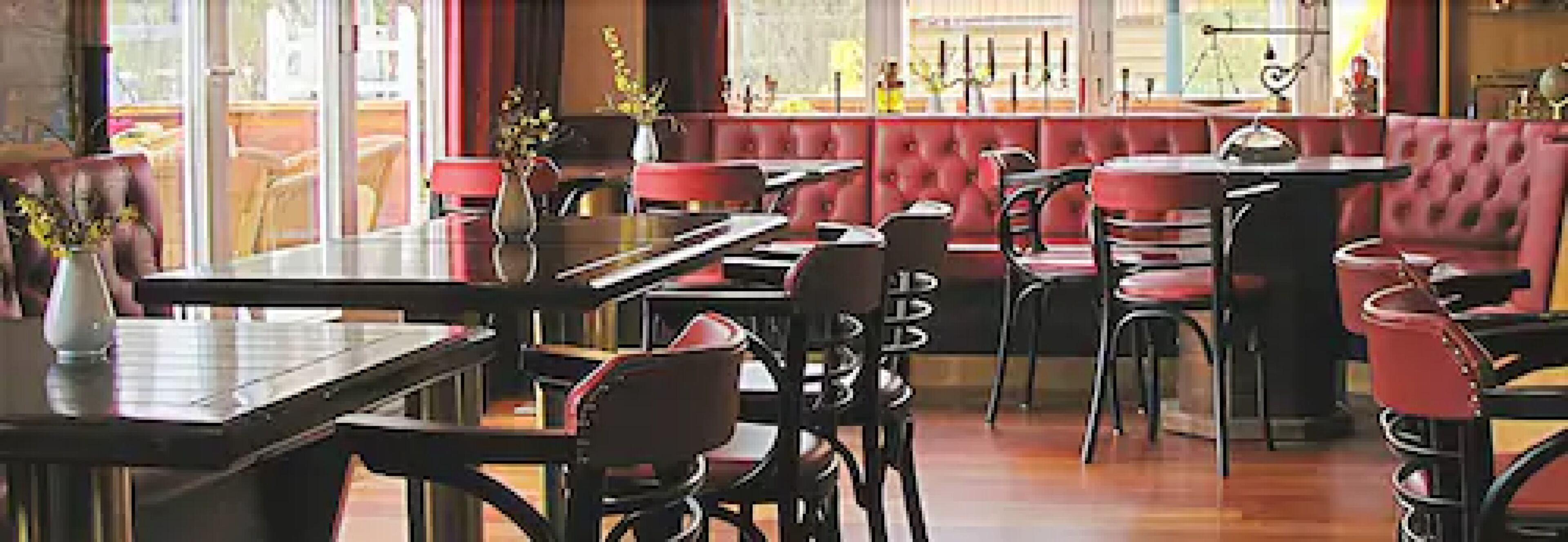 L’intérieur d’un restaurant avec des banquettes et des tables, un plancher en bois et une vue sur l’extérieur par les fenêtres.