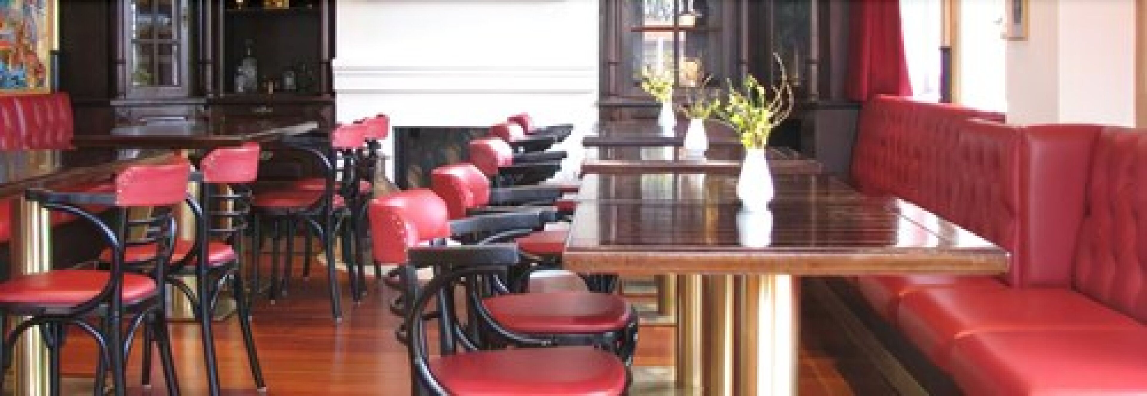 A restaurant with red upholstered booths and chairs, a glass-top table, and a vase with flowers.