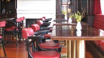 A restaurant with red upholstered booths and chairs, a glass-top table, and a vase with flowers.