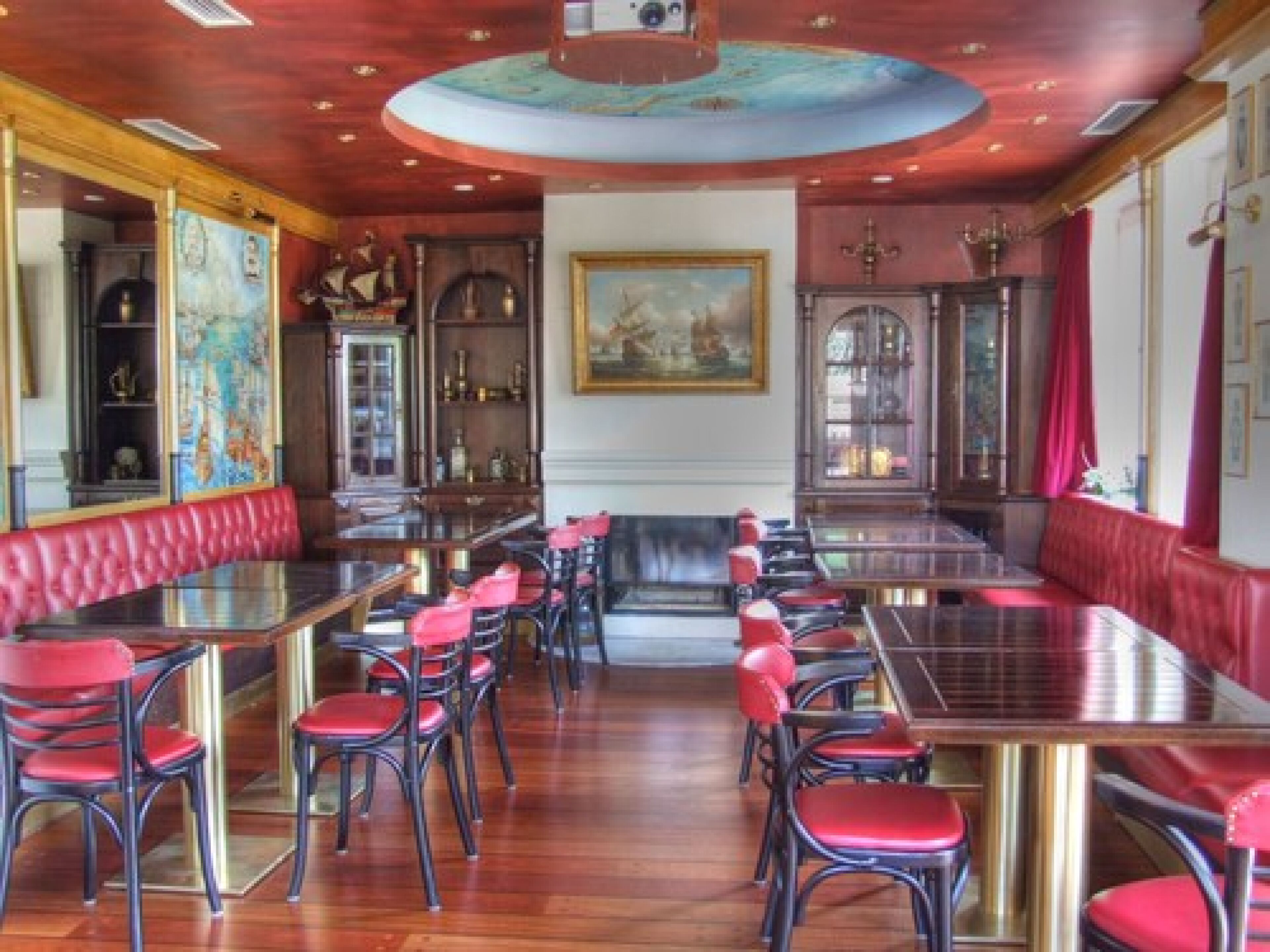 Ein Restaurant mit einem zentralen Essbereich, der rote, gepolsterte Sitzecken und schwarze Stühle bietet, umgeben von Holztischen und -stühlen.