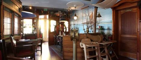 Un restaurante acogedor con muebles de madera, un gran torno giratorio y un mural de un barco en la pared.