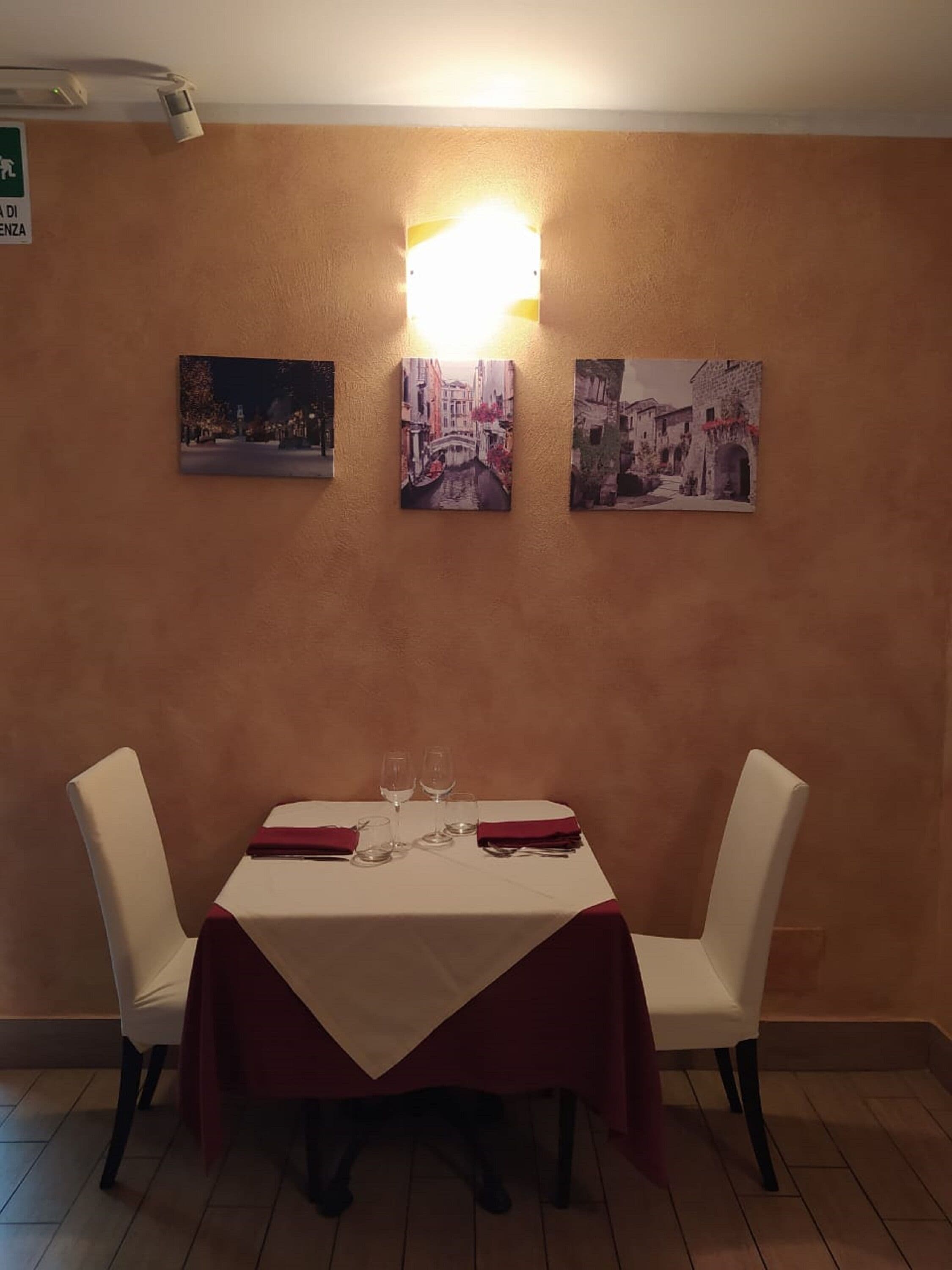 A dining area with a table set for two, chairs, and three framed pictures on the wall.