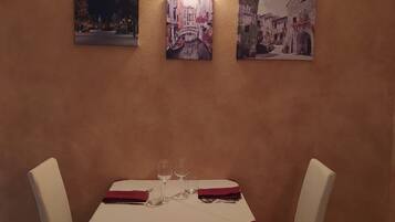 A dining area with a table set for two, chairs, and three framed pictures on the wall.