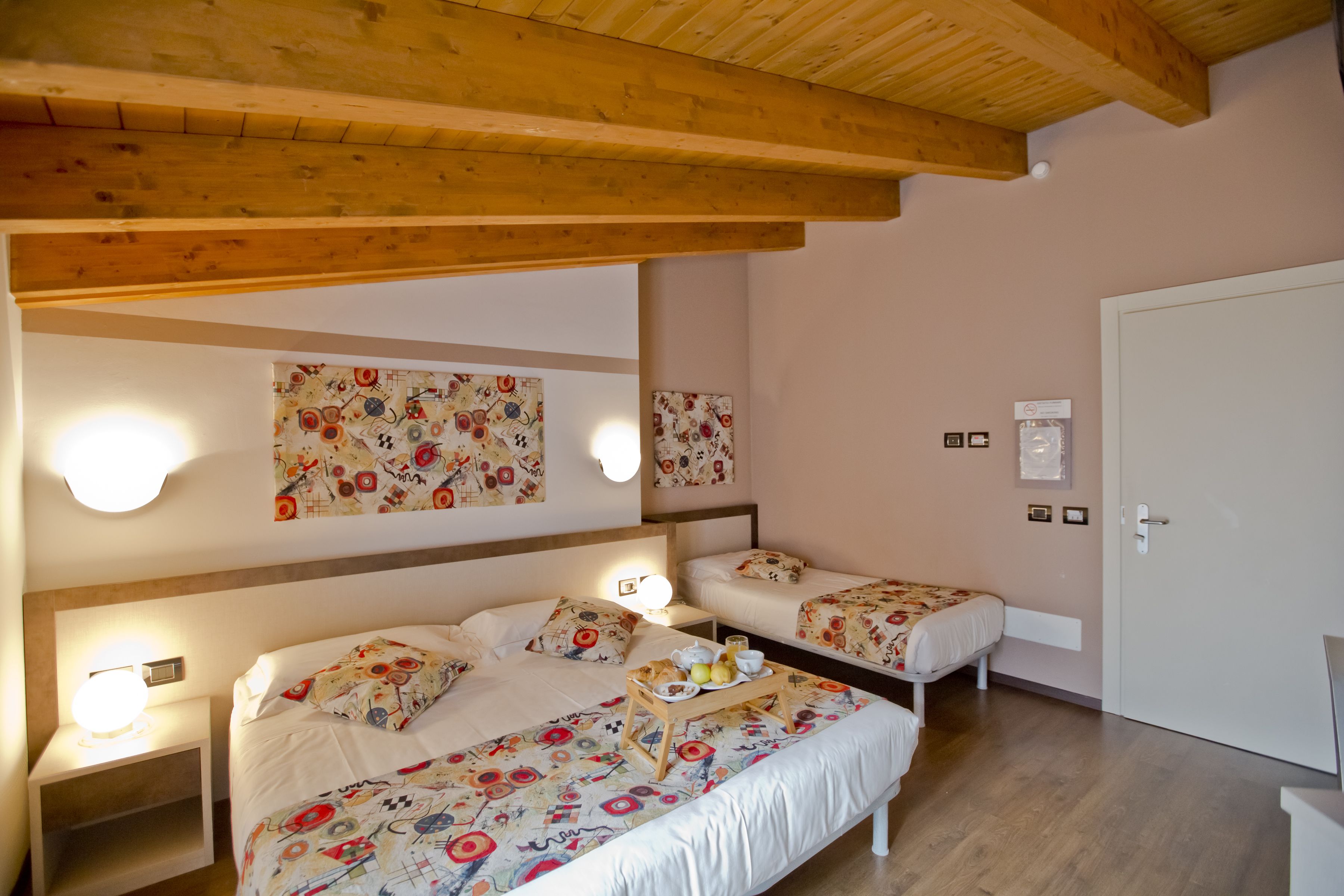 A bedroom with two beds, wooden beams, floral-patterned bedding, bedside lamps, and a tray with fruits and a cup.