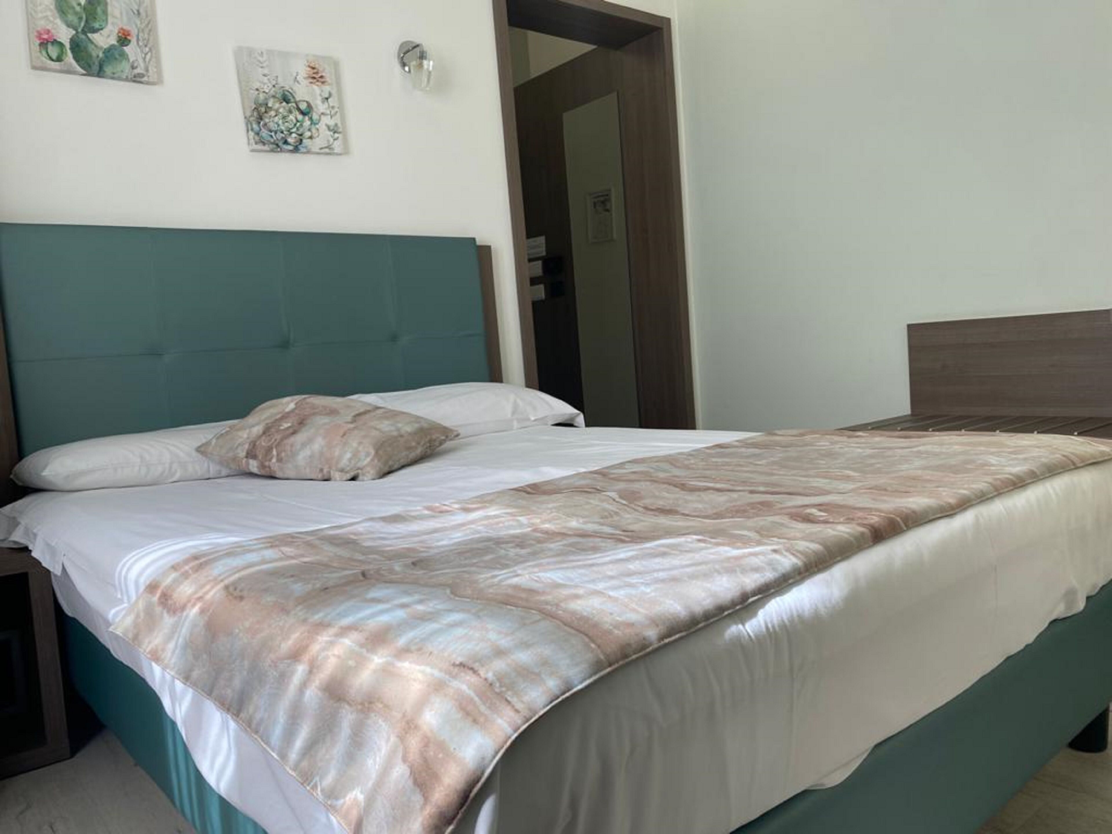 A bedroom with a teal headboard, a bed with a patterned bedspread, and two wall-mounted artworks.
