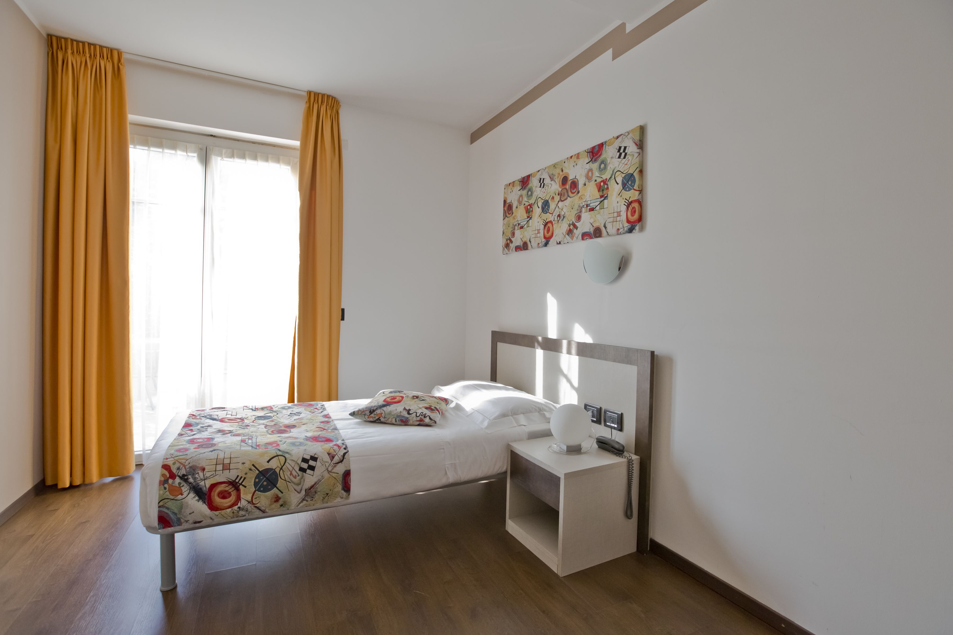 Una habitación de hotel moderna con cama, mesita de noche y una obra de arte colgada en la pared.