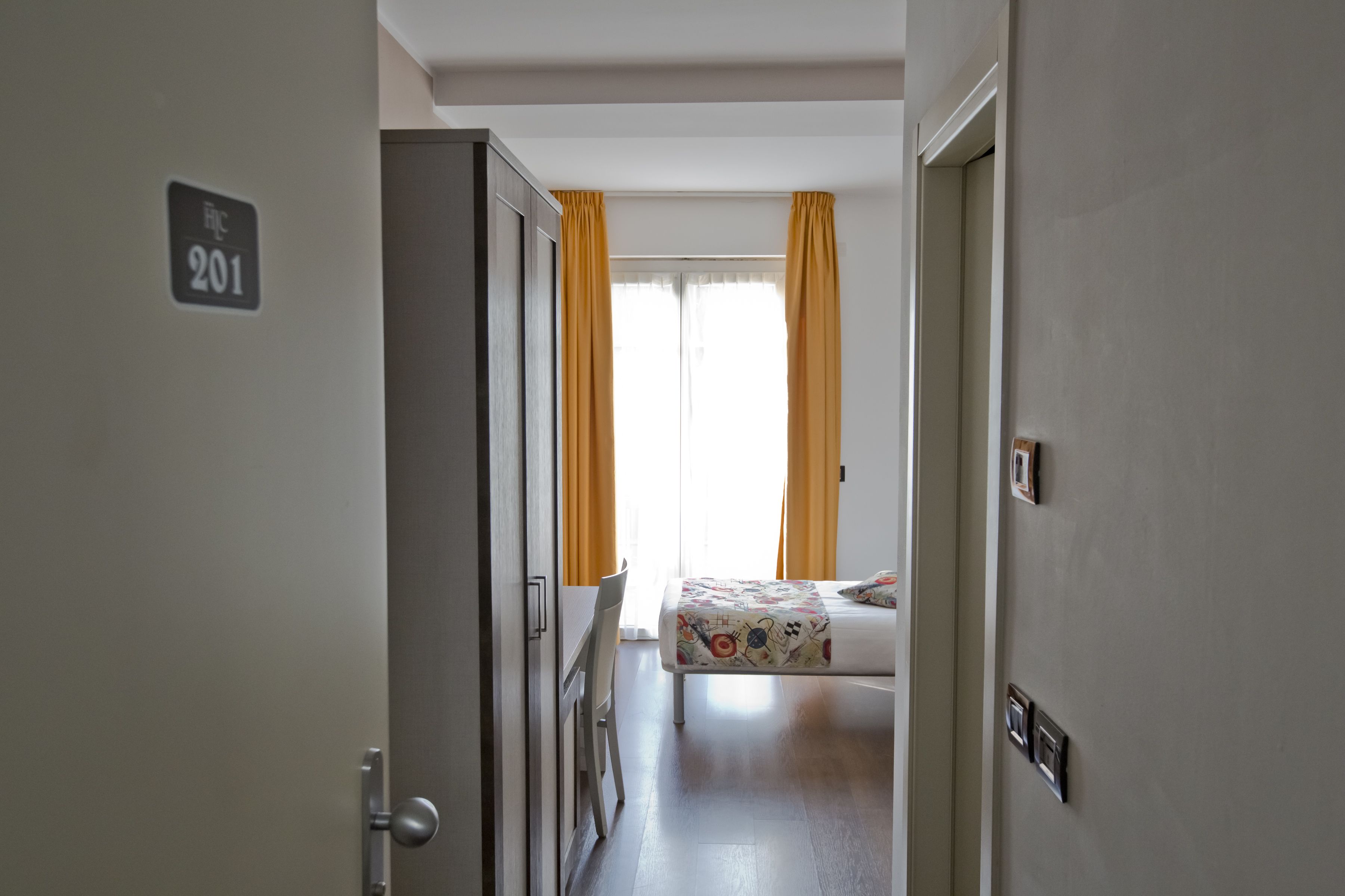 A hotel room with a bed, curtains, and a door with a number sign.