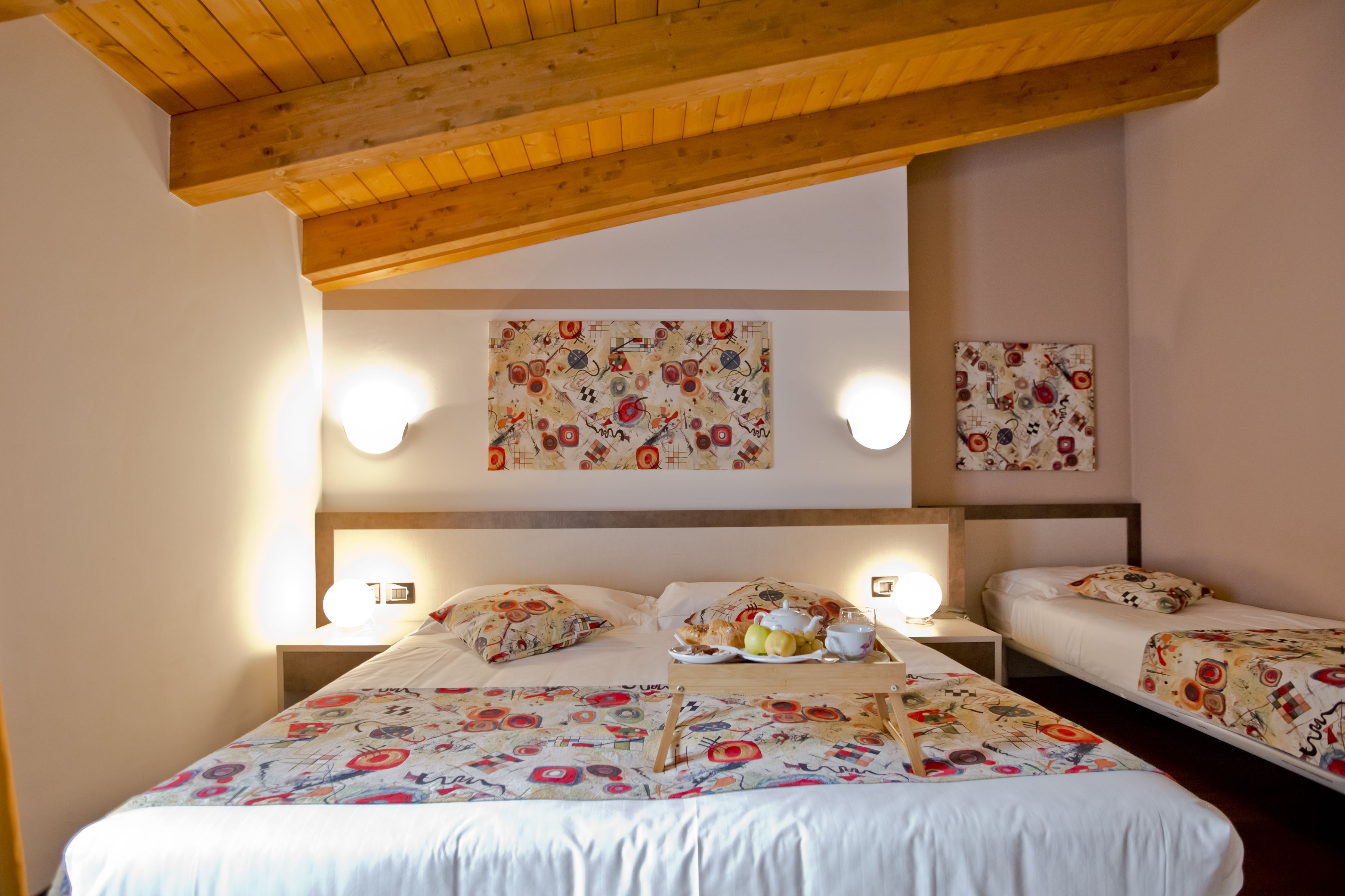 Habitación de hotel con dos camas, vigas de madera en el techo, luces fijadas a la pared y ropa de cama con estampado floral.
