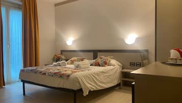 Ein Hotelzimmer mit Bett, Nachttisch und Schreibtisch mit Stuhl. Zwei Wandleuchten befinden sich über dem Bett und ein Fenster mit Vorhängen.
