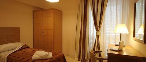 A hotel room with a bed, a desk with a laptop, a chair, a wardrobe, and curtains.