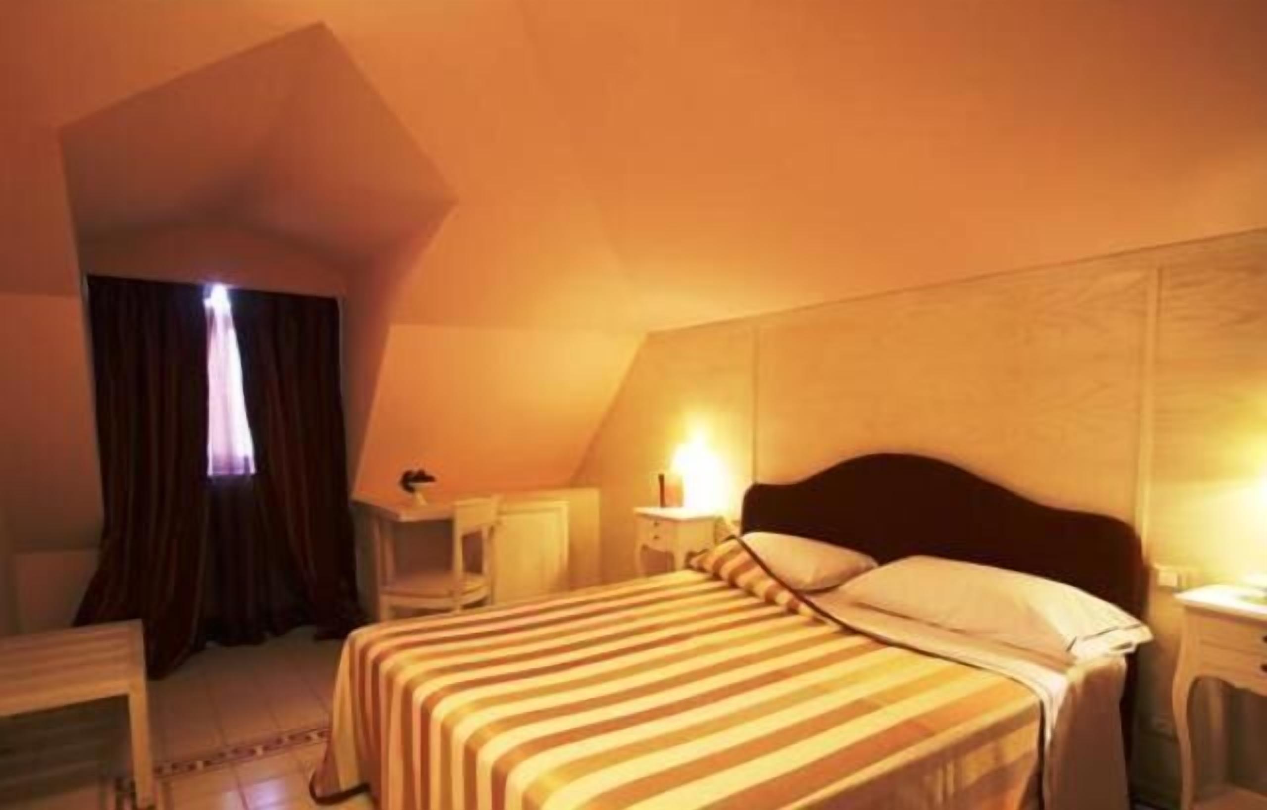 A hotel room with a bed, bedside table, lamp, and a window with curtains.