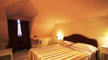 A hotel room with a bed, bedside table, lamp, and a window with curtains.