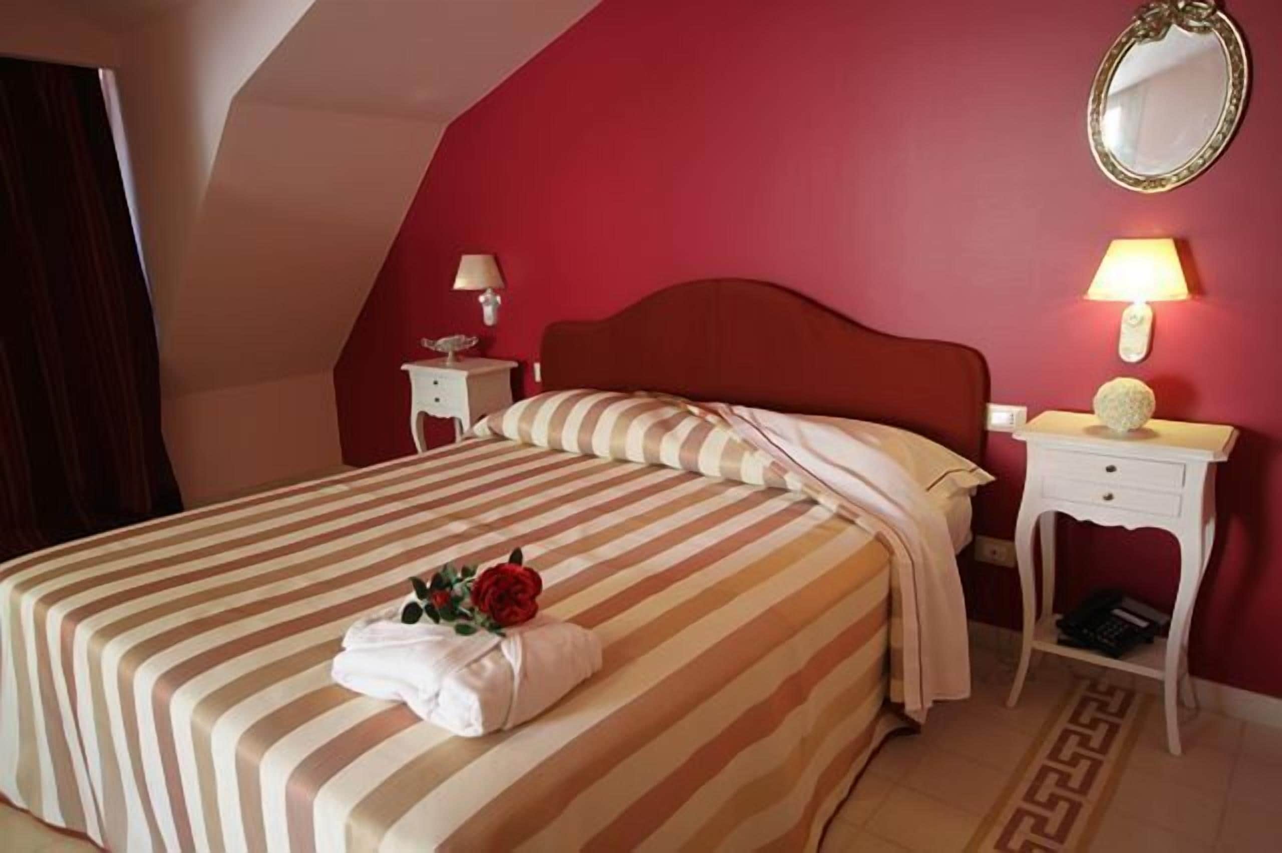 Ein Hotelzimmer mit einem großen Bett, einem Nachttisch mit Lampe, einem Spiegel an der Wand und einem dekorativen Gegenstand auf dem Bett.