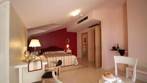 A hotel room with a bed, a desk with a lamp, a chair, a table with a plate of food, and a bottle on a shelf. - Palace Hotel Una Nuova Strada (Nocera Terinese)